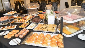 Una mesa de buffet con diversas opciones de comida, incluyendo pasteles, postres, y un cartel que indica que no se permite comida de fuera.