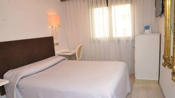 Una habitación de hotel con cama, escritorio, silla, televisión y refrigerador.