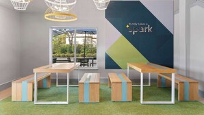 Un espai interior modern amb un mural gran a la paret, diverses taules i bancs, i lluminàries penjants.