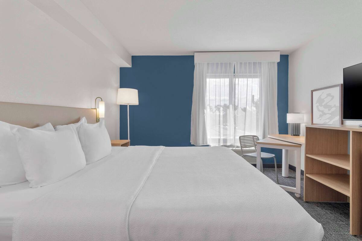 Una habitación de hotel con una cama grande, un escritorio, una silla, un televisor y una ventana con cortinas.