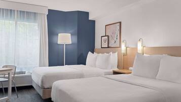 Une chambre d’hôtel avec deux lits, un bureau, une chaise, une lampe et une œuvre d’art encadrée au mur.