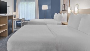 Habitació d'hotel amb dos llits, una taula de treball, televisió i una finestra amb cortines.