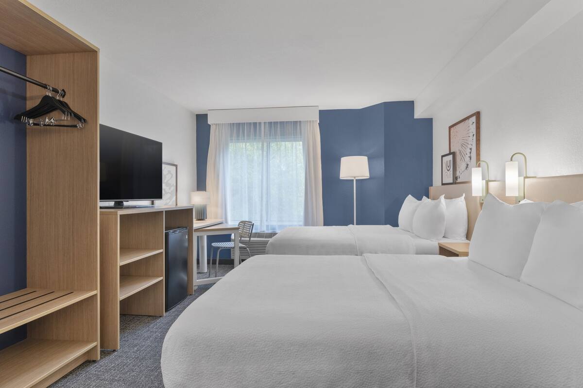 Una habitación de hotel con cama, escritorio, silla, televisor y armario.