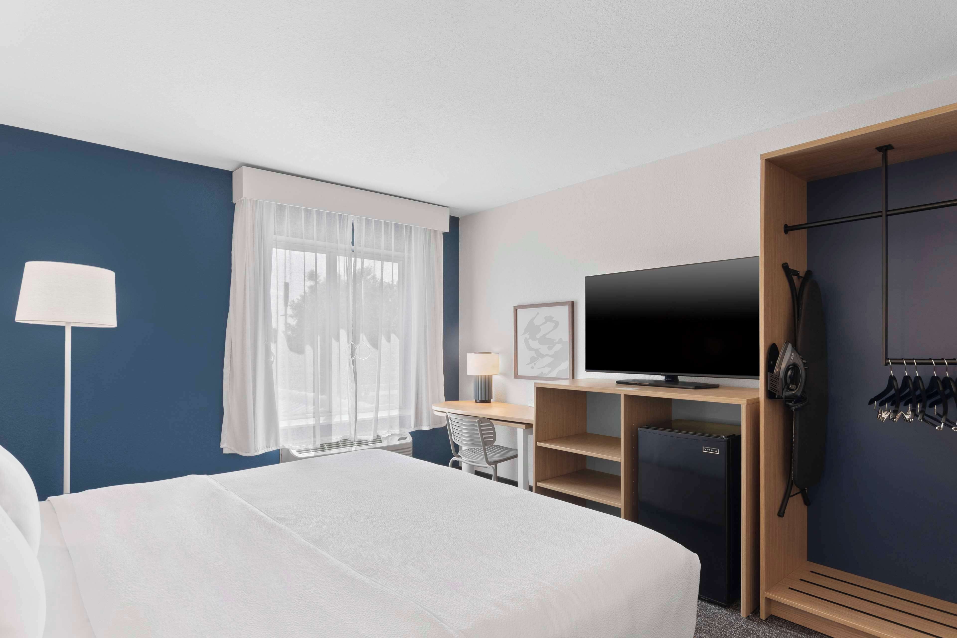 A hotel room with a large bed, a desk with a chair, a television, a wardrobe, and a coat rack.