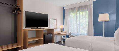 A hotel room with two beds, a desk, a TV, and a window with curtains.