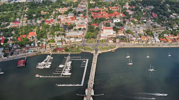 An aerial view of a coastal town with a marina, docked boats, and a bridge connecting the land to the water. - Holiday Inn Express St. Augustine near Dtwn - Historic by IHG (St. Augustine)