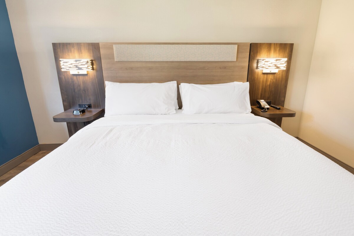 A neatly made bed with white linens, two bedside tables with lamps, and a wooden headboard.