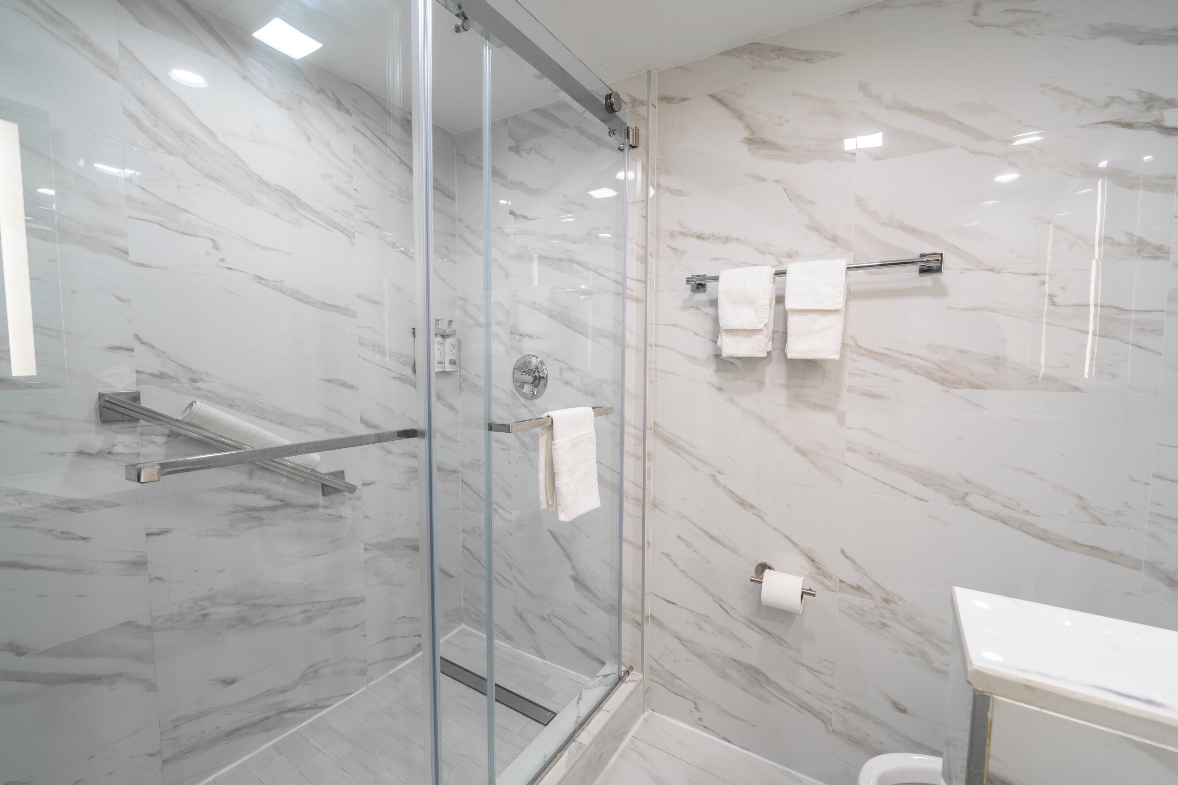 A modern bathroom with a glass-enclosed shower, marble walls, and a white sink.