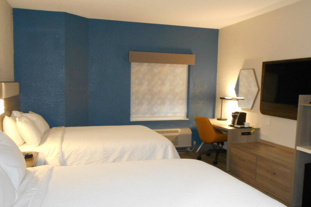 A hotel room with two beds, a desk, a chair, a television, and a microwave.
