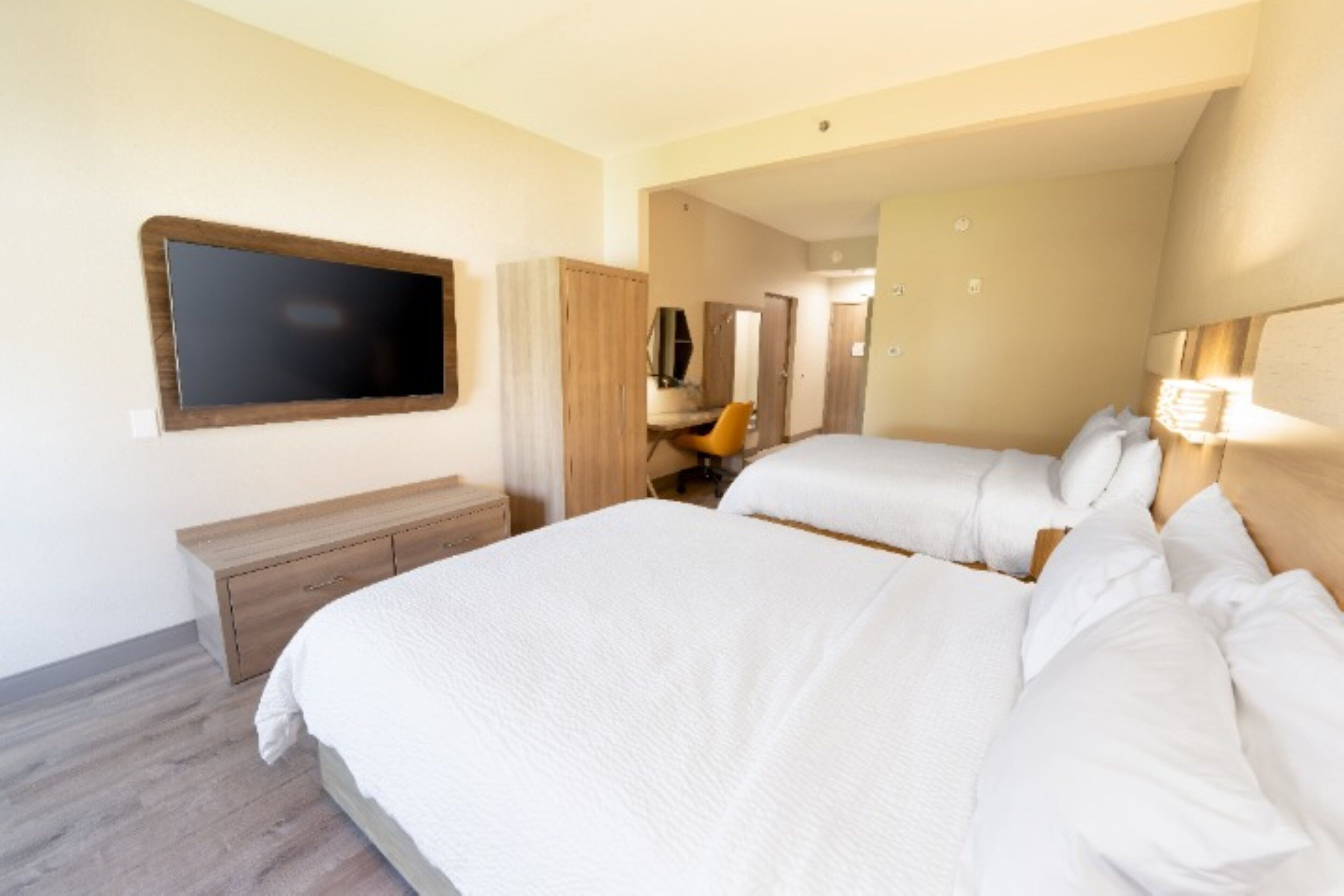 Habitación de hotel con una cama grande, un televisor montado en la pared, un escritorio con una silla y un armario.