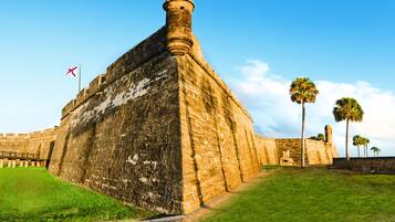 Una fortaleza histórica con una bandera, palmeras y un cielo despejado.