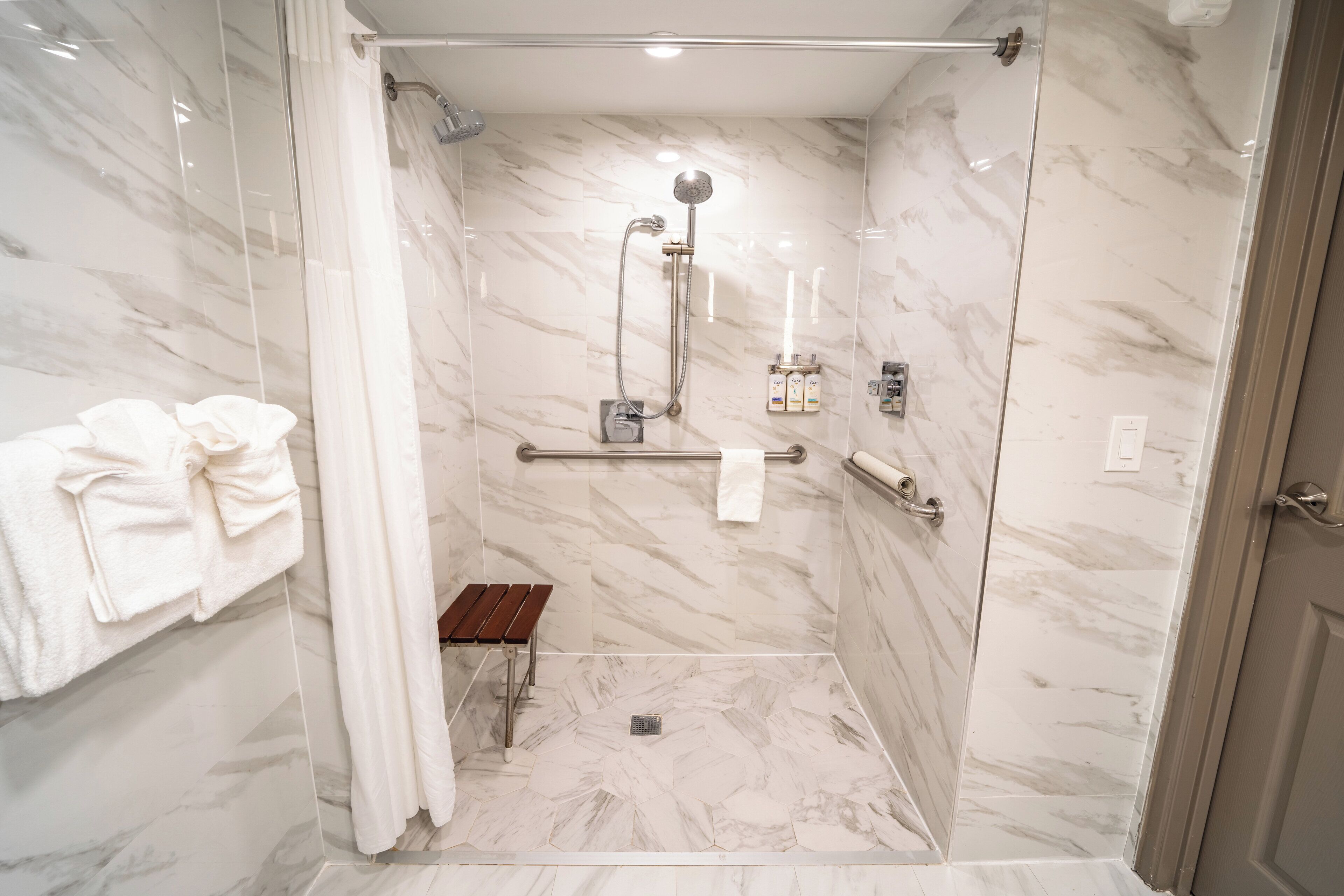 Une salle de bain moderne avec une douche à parois de verre, des murs en marbre, un porte-serviettes et un banc.