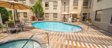 A pool area with a tiled deck, lounge chairs, and umbrellas.