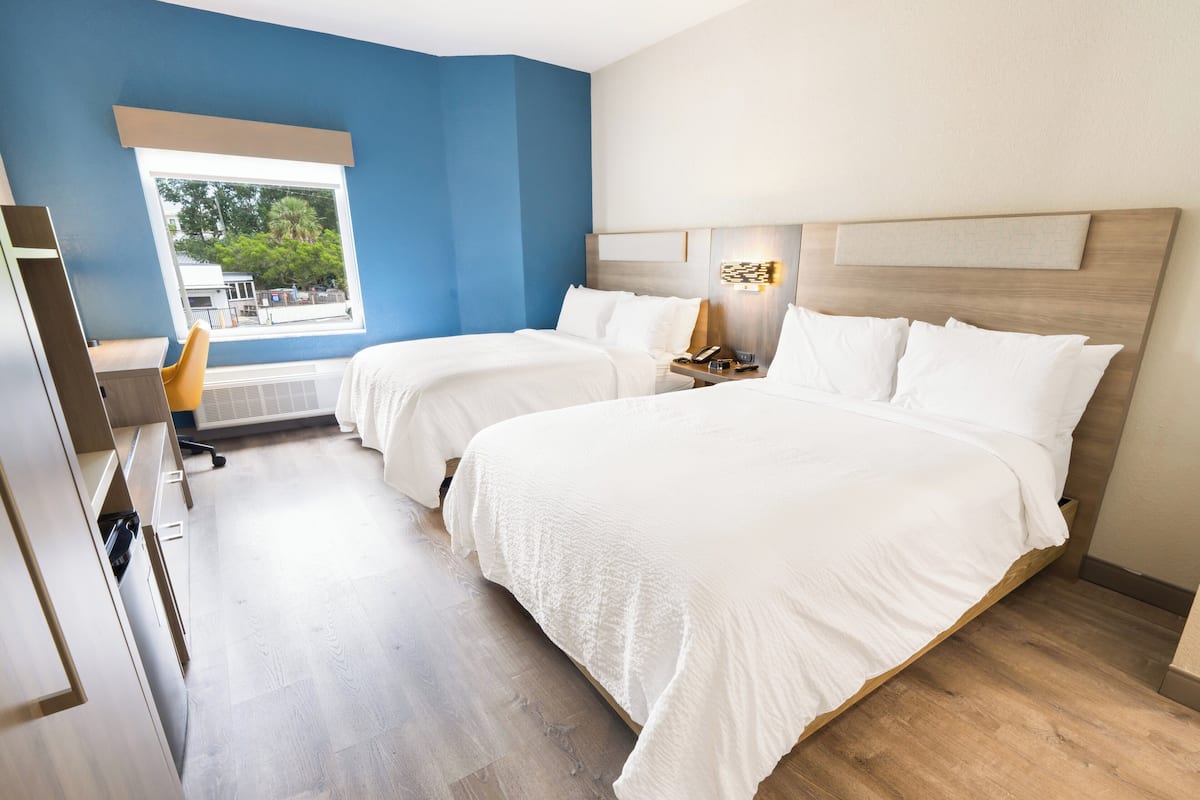 A hotel room with two beds, a desk, and a chair.