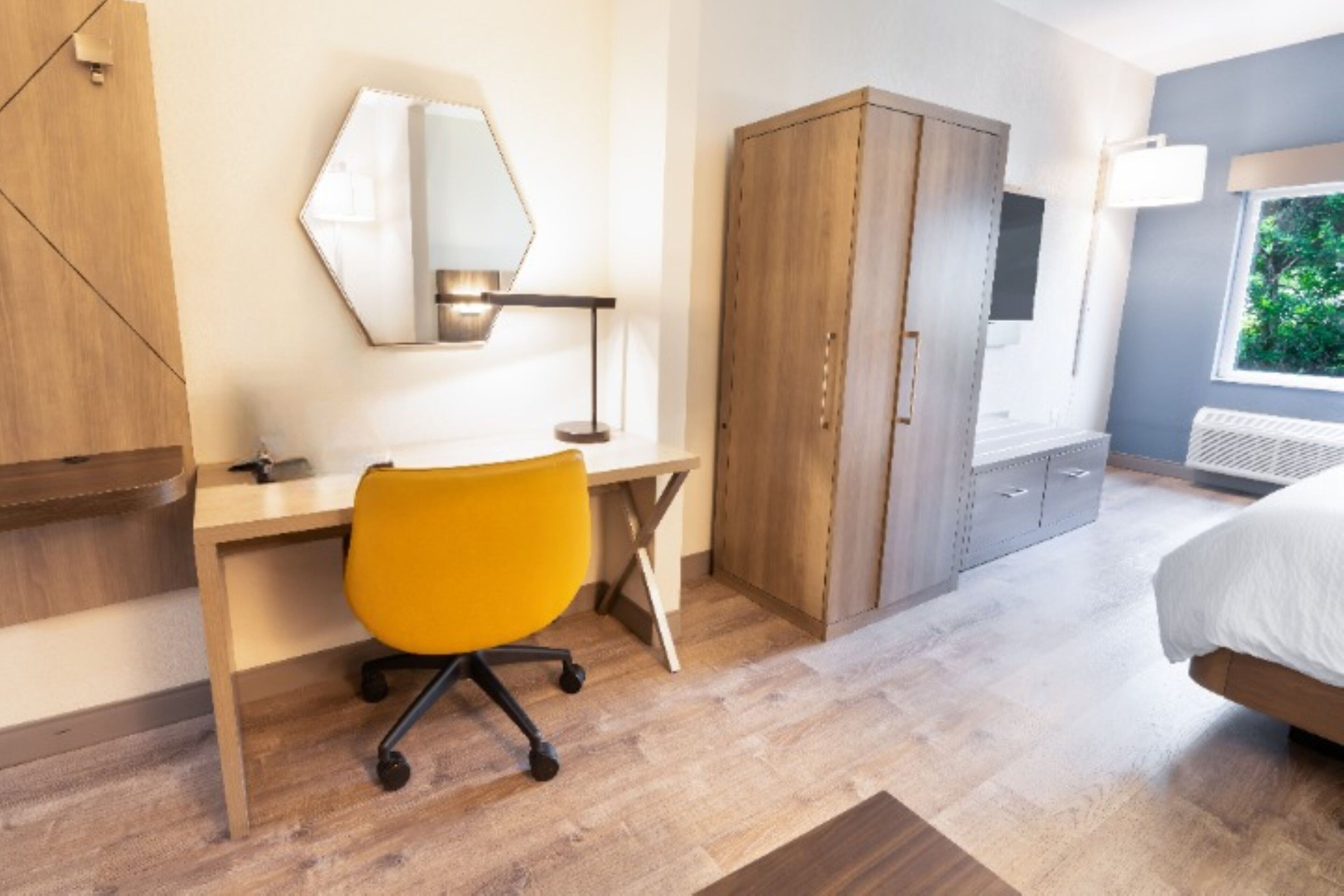 A modern bedroom with a wooden desk, a yellow office chair, a wardrobe, and a bed.