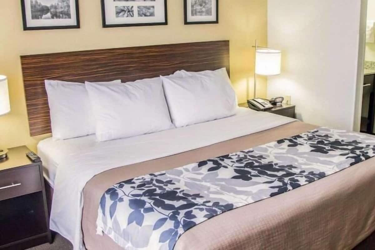 Una cama bien hecha con sábanas blancas, un plaid estampado de flores y un cabecero de madera.