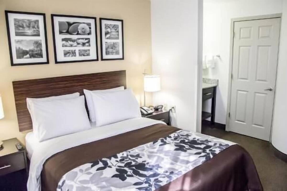 Una habitación de hotel con una cama, una mesita de noche, una lámpara, un escritorio y una puerta.