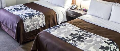 A hotel room with two beds, each with a floral-patterned bedspread, a wooden headboard, a bedside table with a lamp, and a phone.