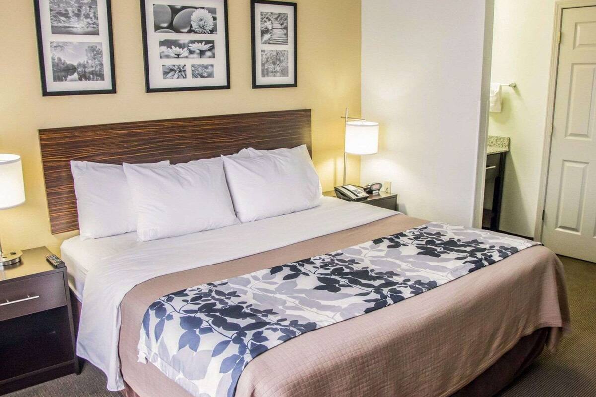 Habitación de hotel con cama, lámparas de noche, mesita de noche, teléfono y tres cuadros en la pared.