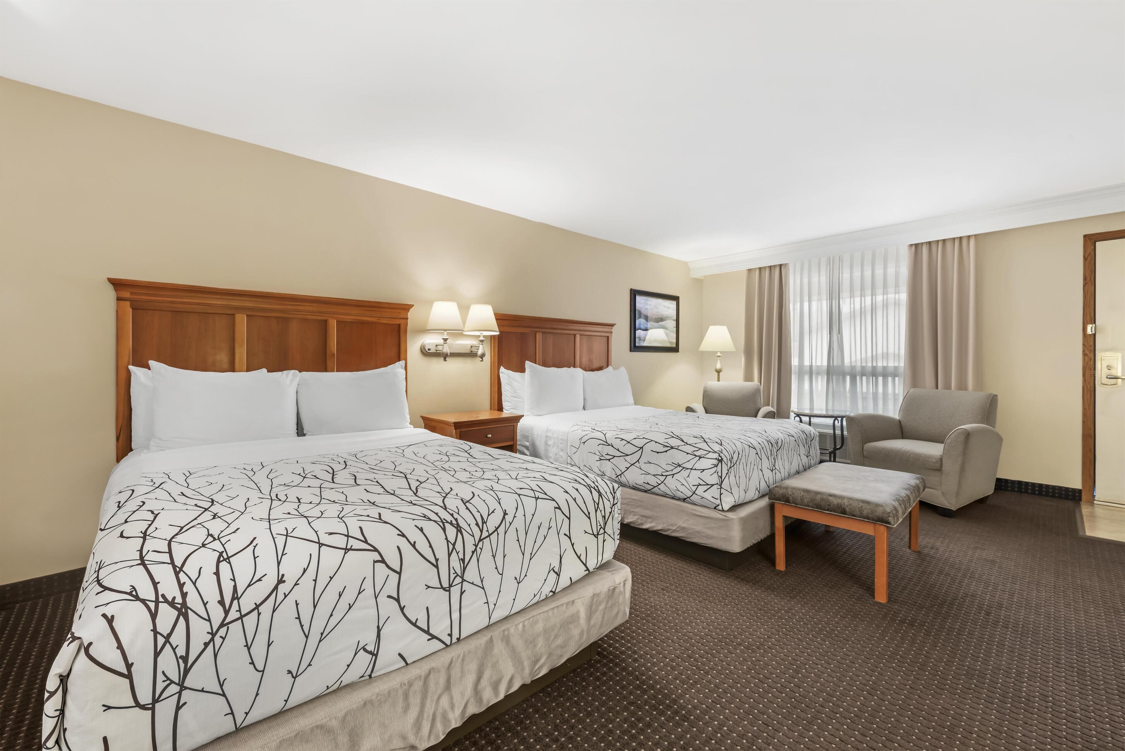A hotel room with two beds, a chair, a small table, and a nightstand.