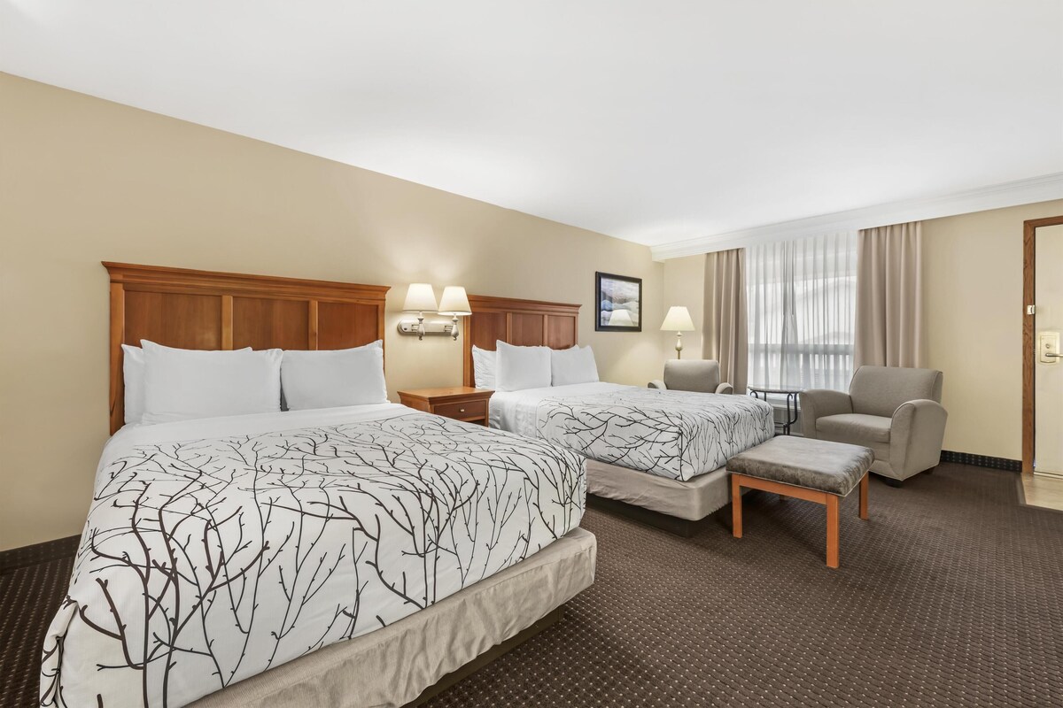 A hotel room with two beds, a chair, a small table, and a nightstand.