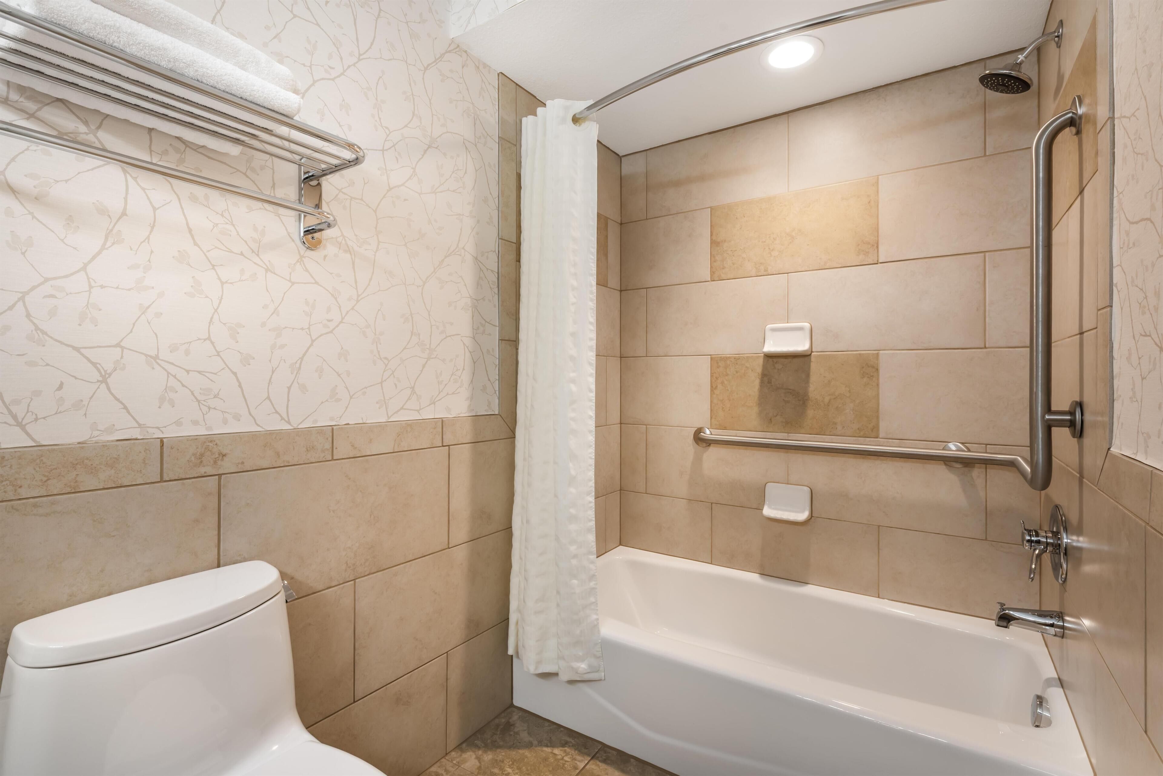 Un baño con inodoro, ducha con barra de apoyo y bañera.