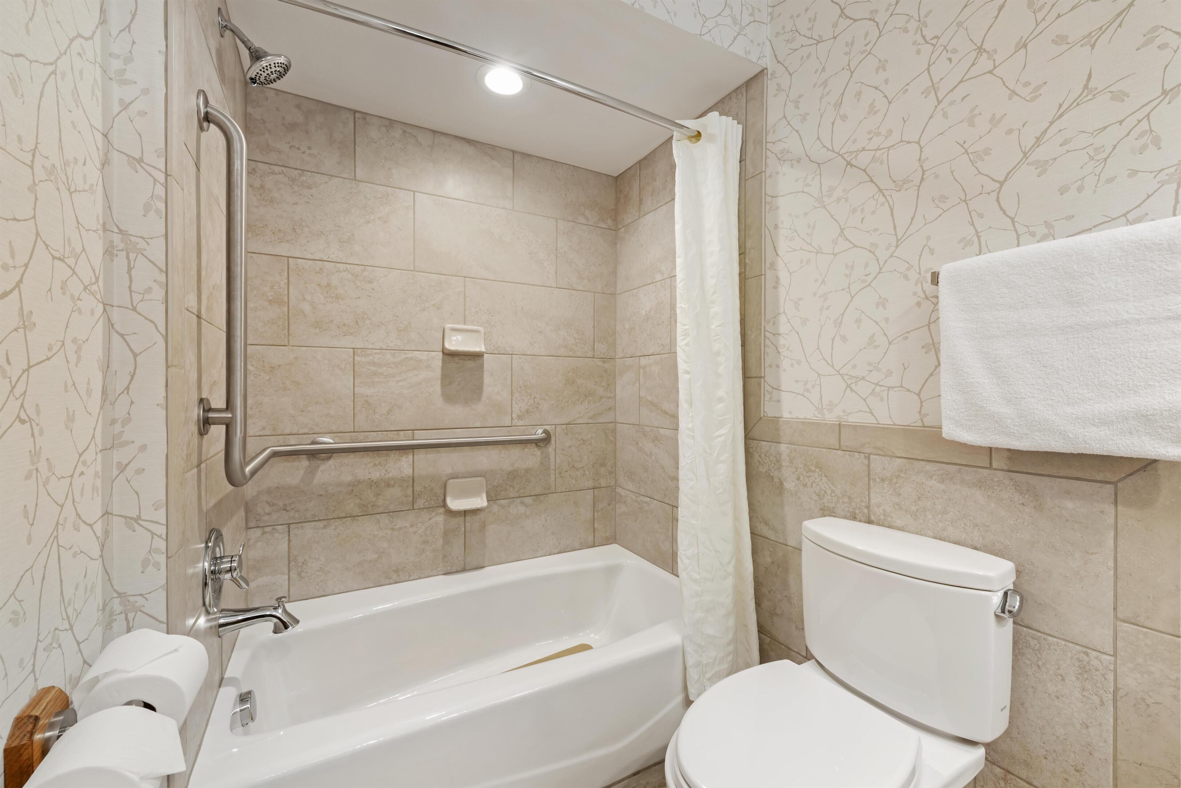 Un baño con bañera, inodoro, barras de apoyo y cabezal de ducha.