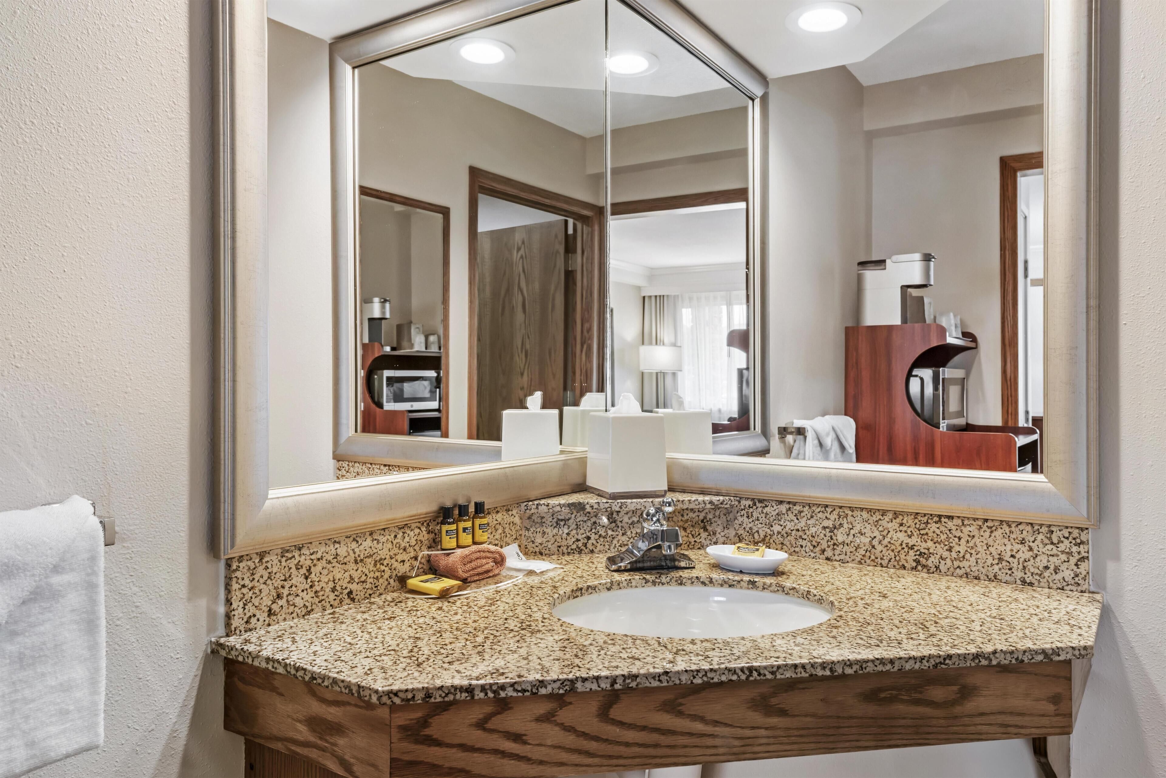 A bathroom with a granite countertop, a sink, a mirror, and a wooden vanity.