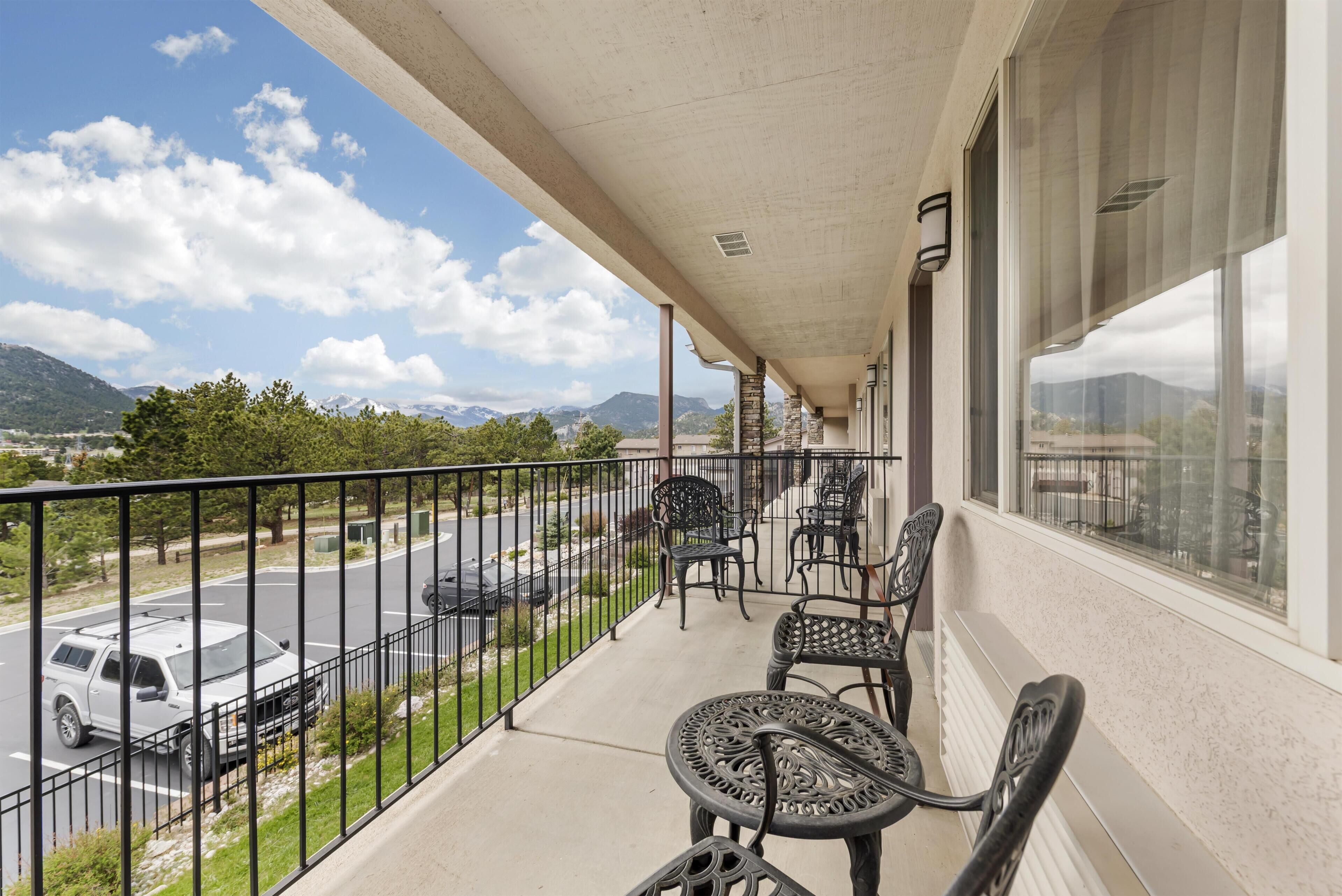 A balcony with outdoor seating, a view of a parking lot, and mountains in the background.