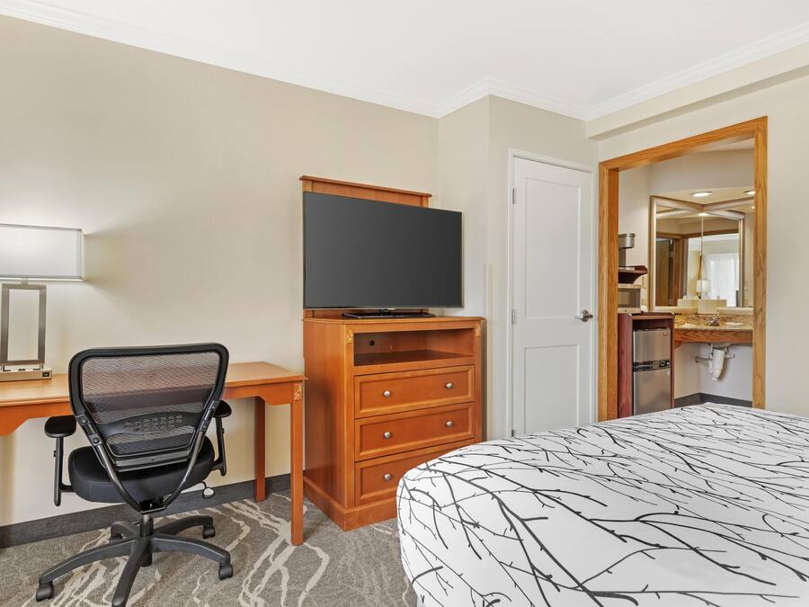 A hotel room with a bed, desk, chair, TV, dresser, and a bathroom visible through an open door.