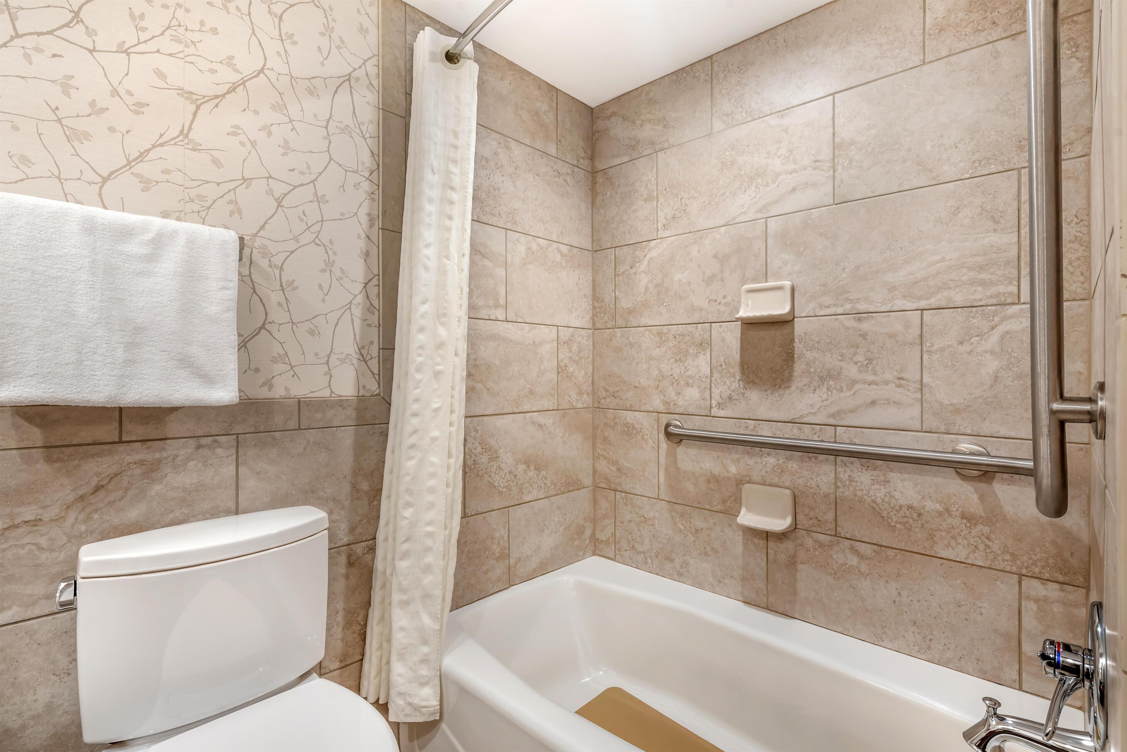 A bathroom with a toilet, bathtub, shower curtain, and tiled walls.