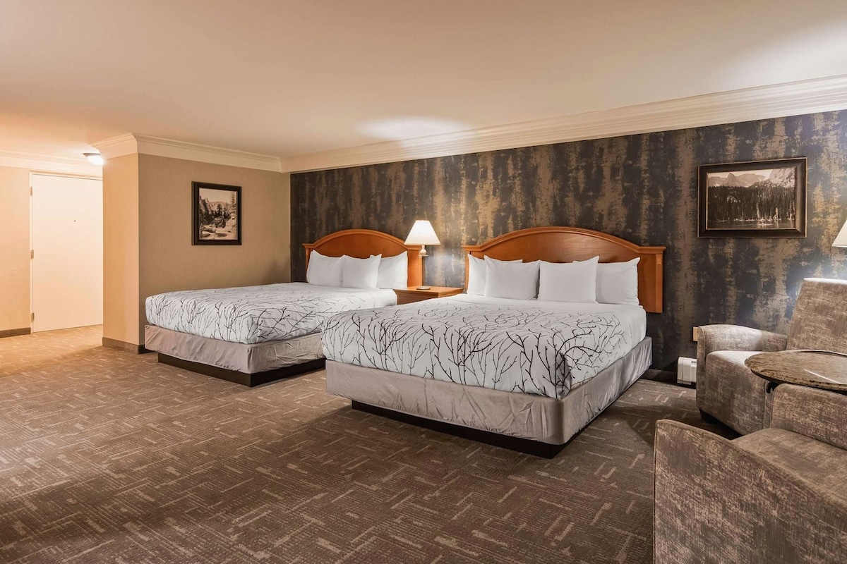 A hotel room with two beds, a chair, a small table, and a lamp.