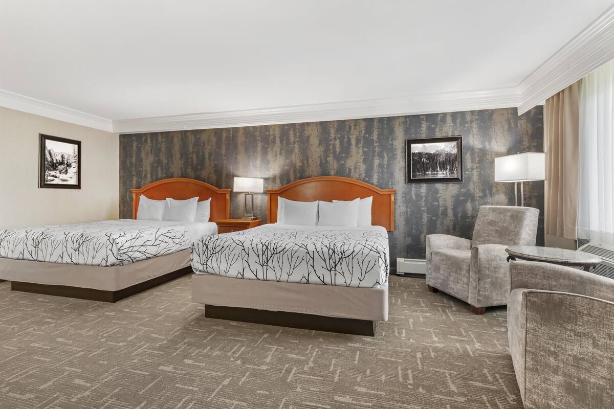 Une chambre d’hôtel avec deux lits, une chaise, une table et deux lampes fixées au mur.