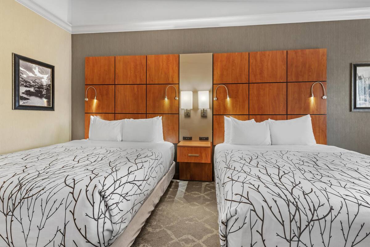 Une chambre d’hôtel avec deux lits, une tête de lit en bois, un miroir, des lampes de chevet et un tableau encadré au mur.