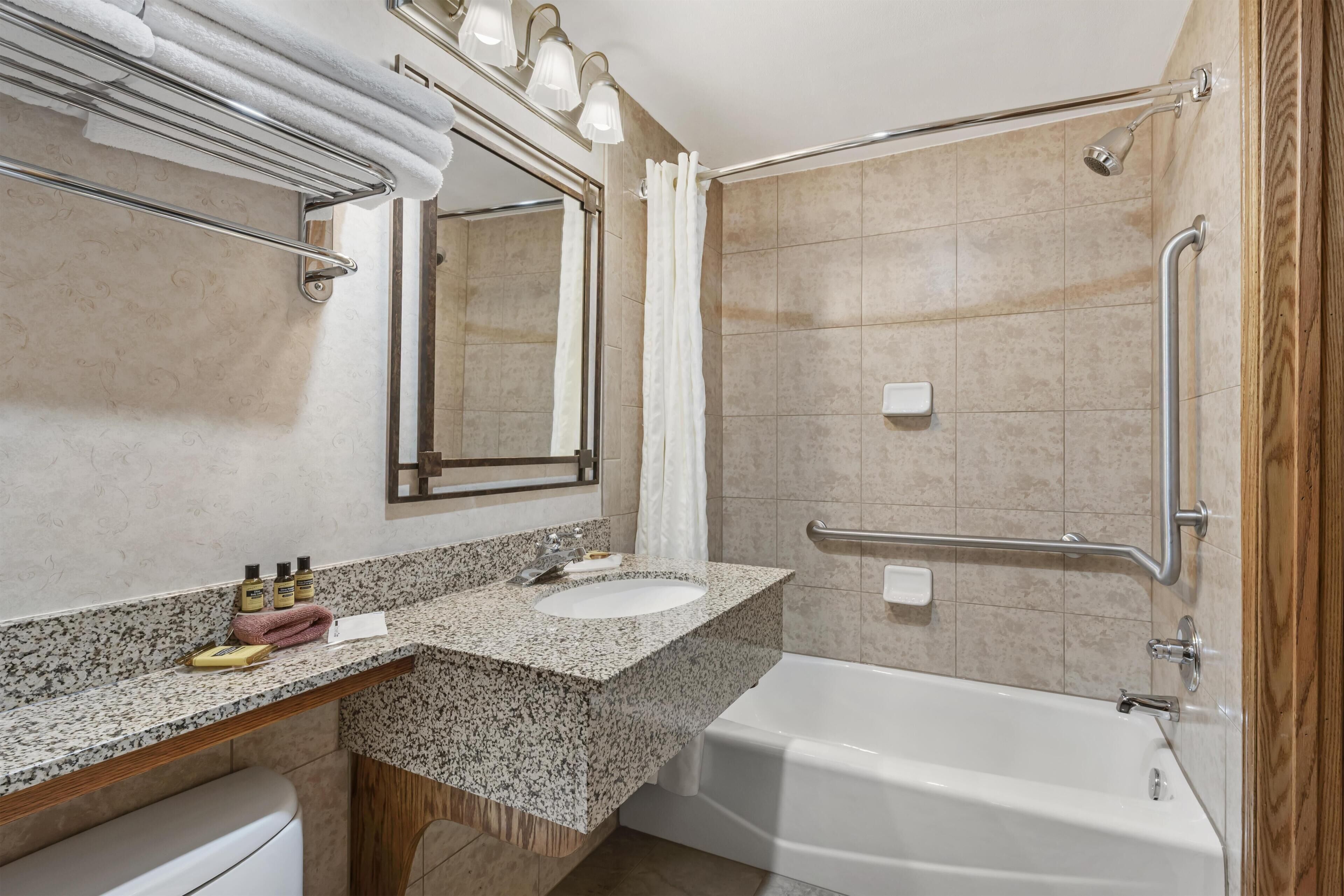 Een badkamer met wastafel, spiegel, douche en handgrepen.