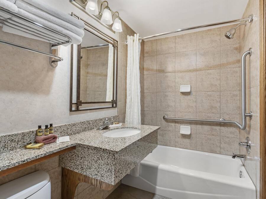 Ein Badezimmer mit Waschbecken, Spiegel, Dusche und Haltegriffen.