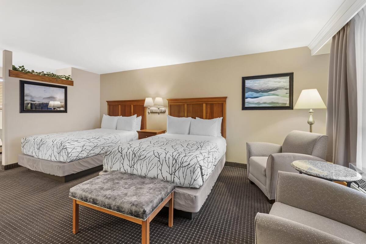 Une chambre d’hôtel avec deux lits, un canapé, une petite table et un banc.