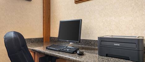 A desk with a computer, keyboard, mouse, and printer in a room with a window and a framed picture on the wall.