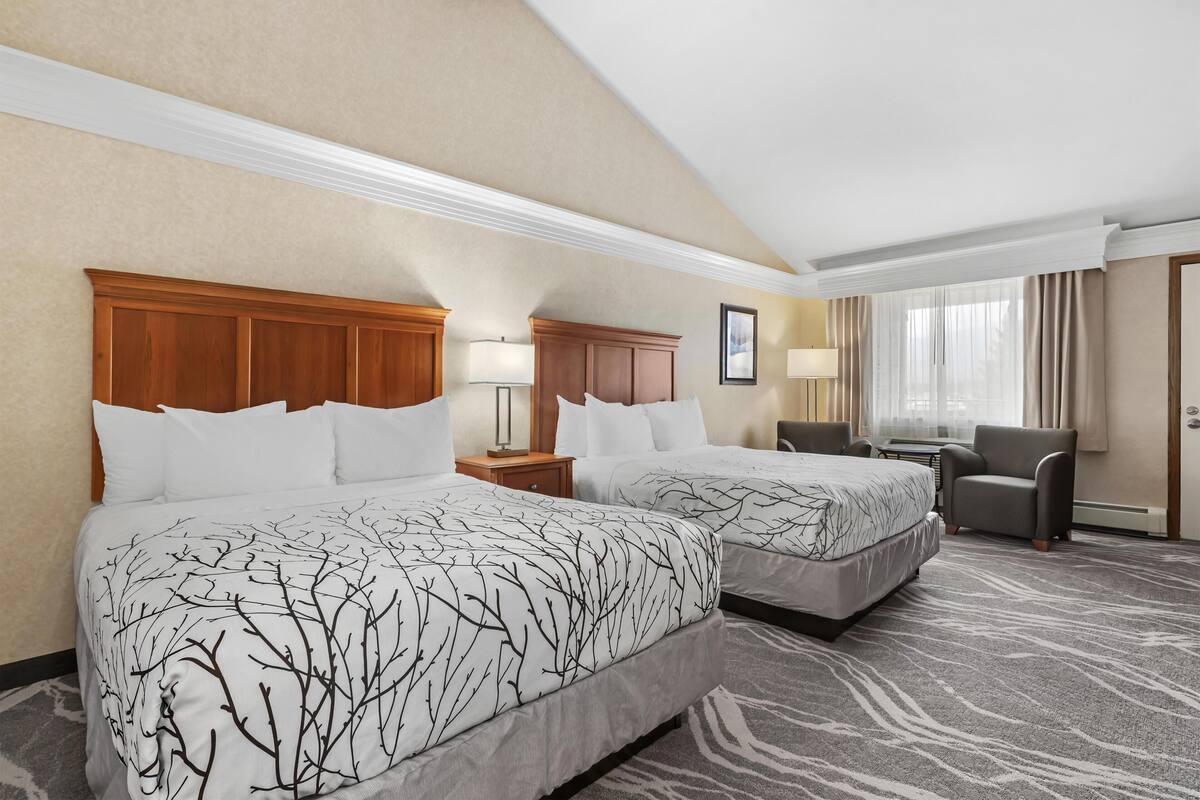 Une chambre d’hôtel avec deux lits, un bureau, une chaise et une fenêtre avec des rideaux.