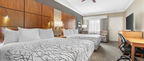 A hotel room with a large bed, a desk, a chair, a television, and a ceiling fan.