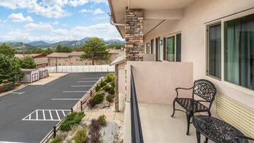 A hotel with a parking lot, a balcony with a chair, and a mountain view.