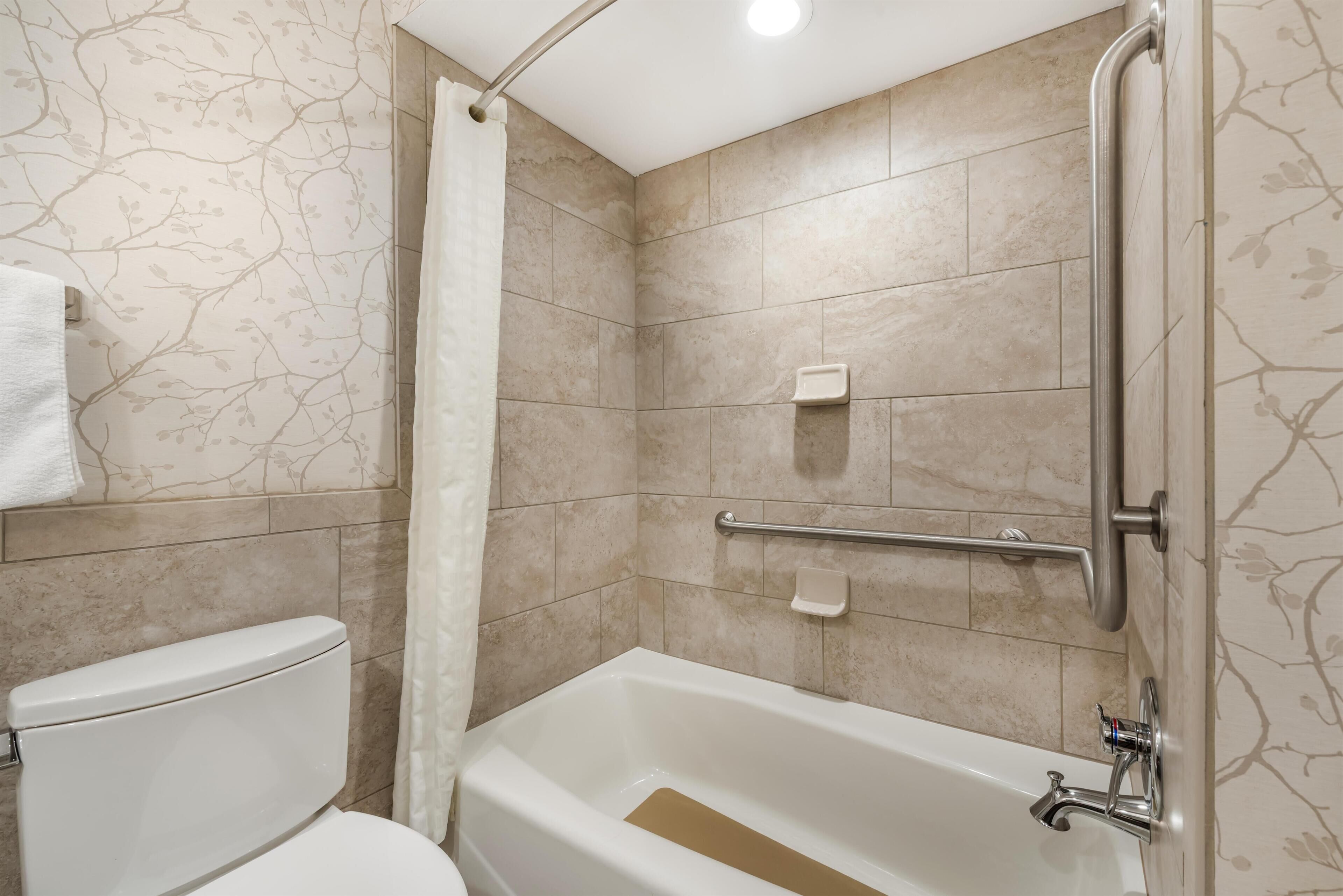 Une salle de bain équipée de toilettes, d’une baignoire, d’un rideau de douche et de barres d’appui.