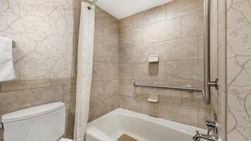 Une salle de bain équipée de toilettes, d’une baignoire, d’un rideau de douche et de barres d’appui.