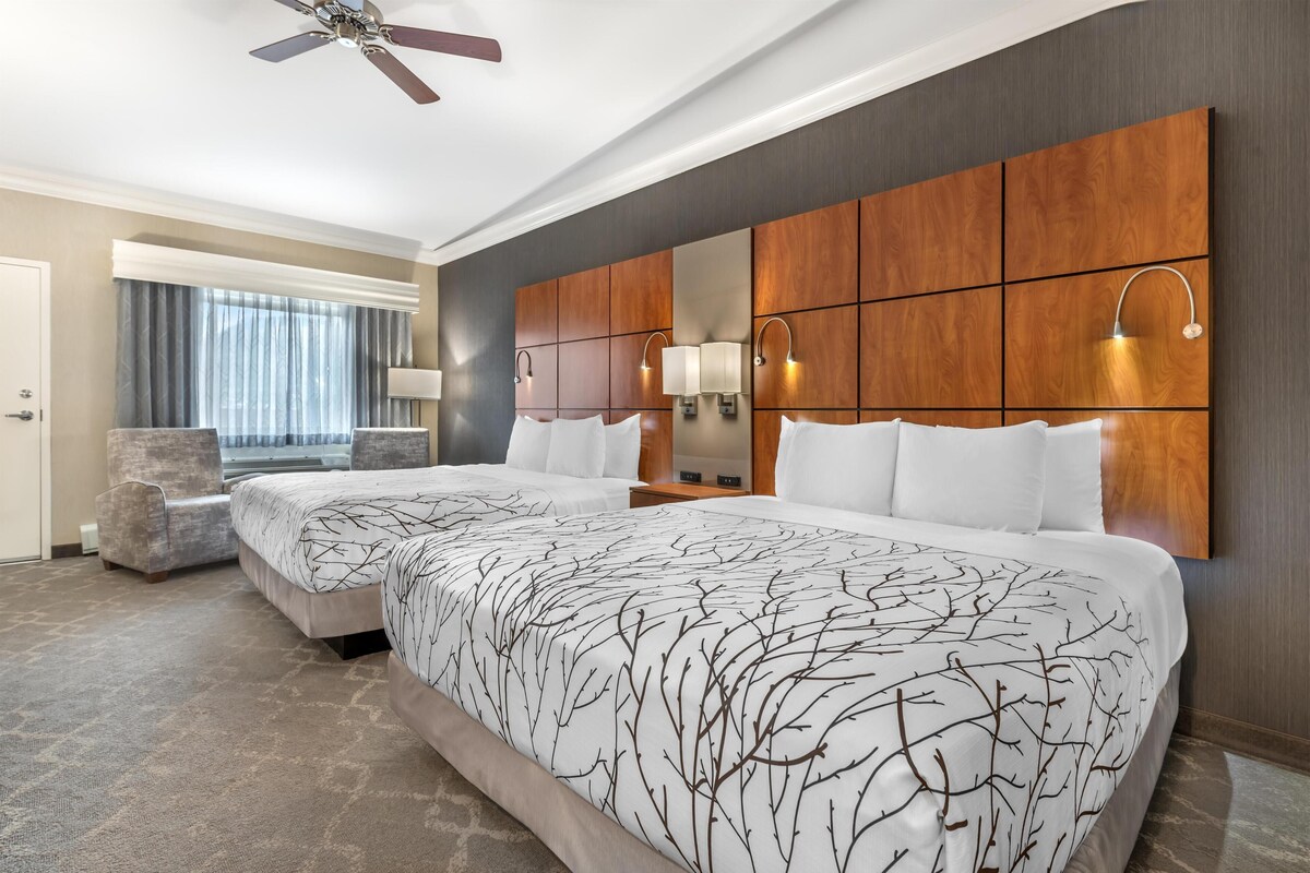 A hotel room with two beds, a seating area, a ceiling fan, and a large mirror.