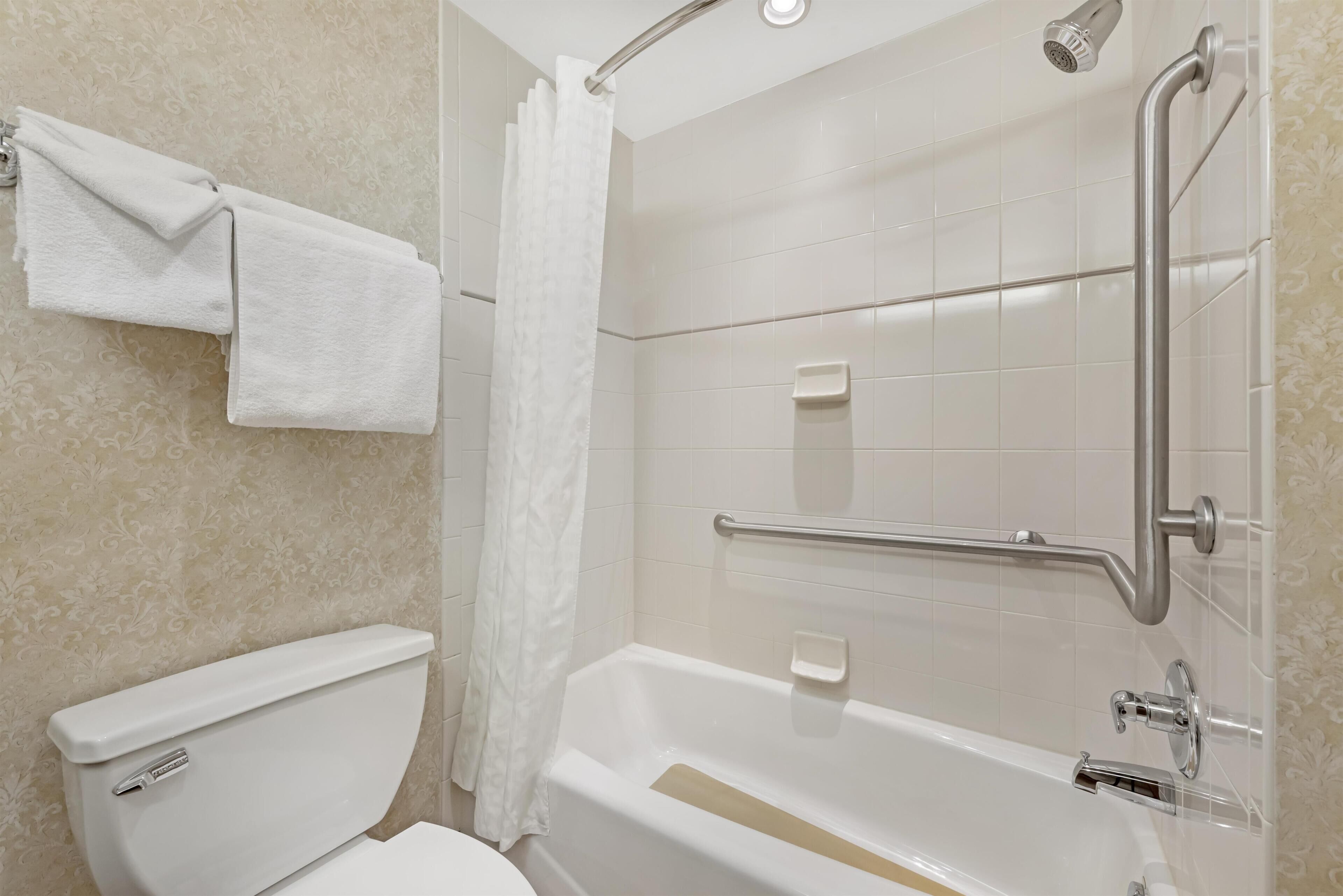 Een badkamer met toilet, bad, douche en een handgreep.