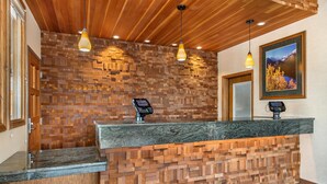 A reception desk with a wooden wall design, two pendant lights, a framed picture on the wall, and a digital display. - Best Western Plus Silver Saddle Inn (Estes Park)