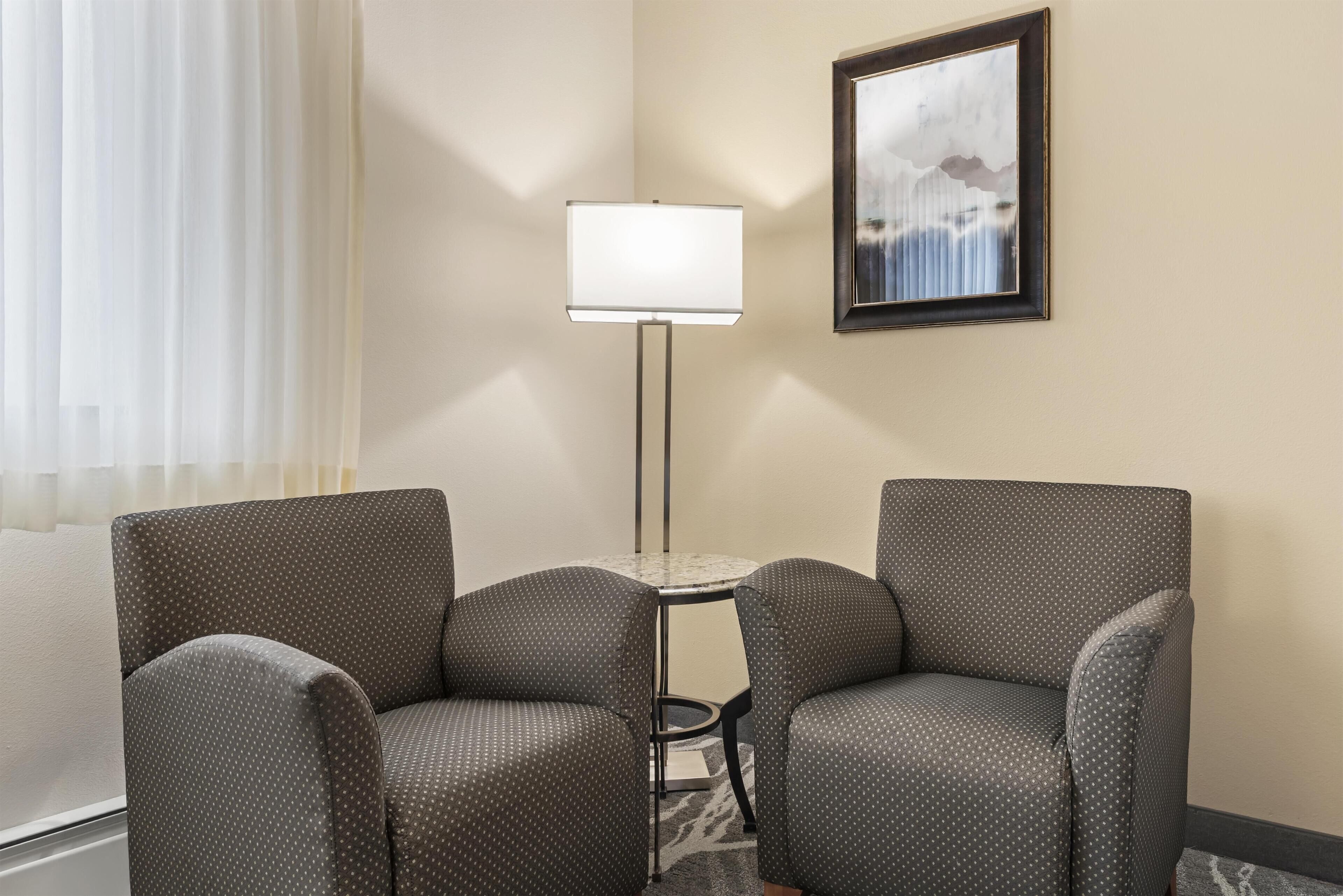 A hotel room with two armchairs, a floor lamp, a small table, and a framed picture on the wall.
