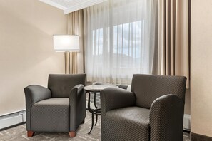 A hotel room with two armchairs, a small table, a lamp, and a view through sheer curtains. - Best Western Plus Silver Saddle Inn (Estes Park)