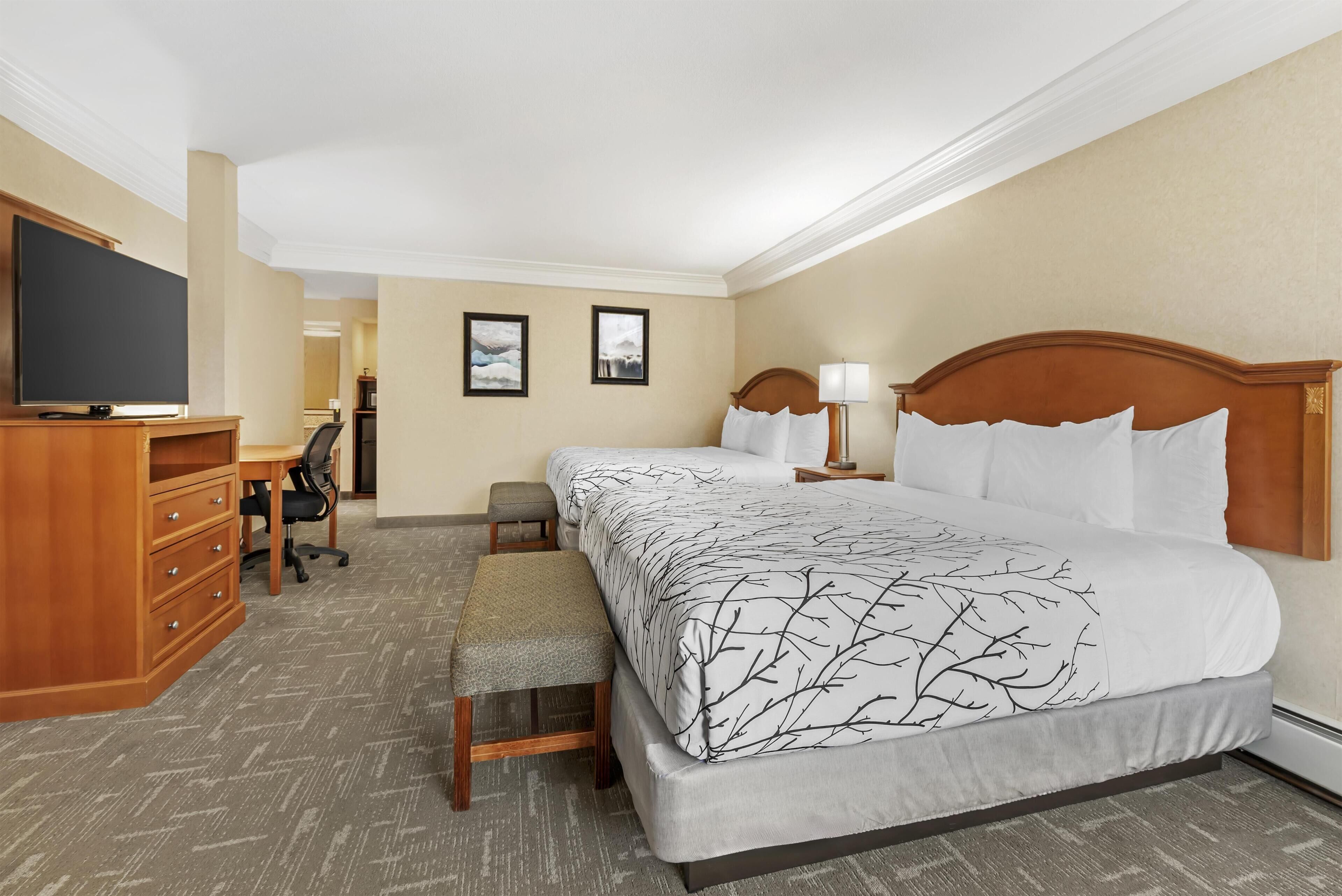 A hotel room with a bed, a desk, a television, and a bench.