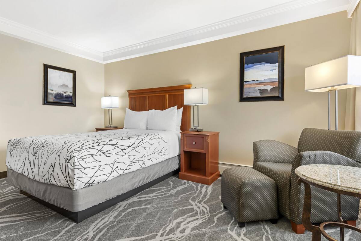 Une chambre d’hôtel comprenant un lit, deux tables de chevet, une chaise, une table et deux lampes fixées au mur.